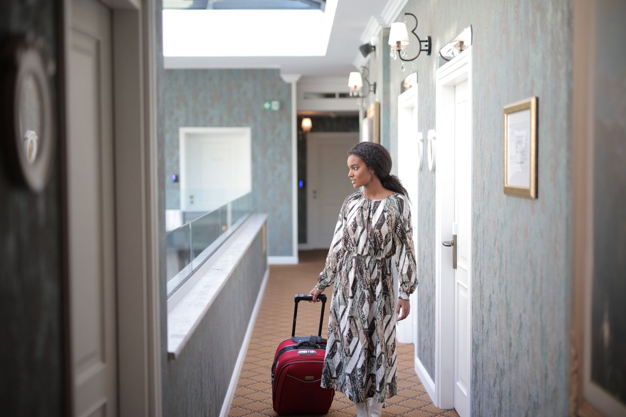 Services A woman walks with luggage through a stylish hotel corridor, embodying travel elegance.