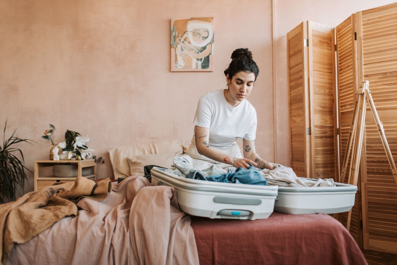 Services A woman packing her suitcase with clothes in a stylish and cozy bedroom setting.